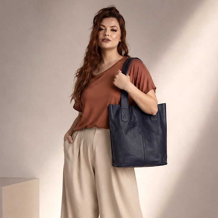 Mulher usando a bolsa de ombro grande azul marinho, destacando o caimento macio do couro e o vão livre de 21cm.