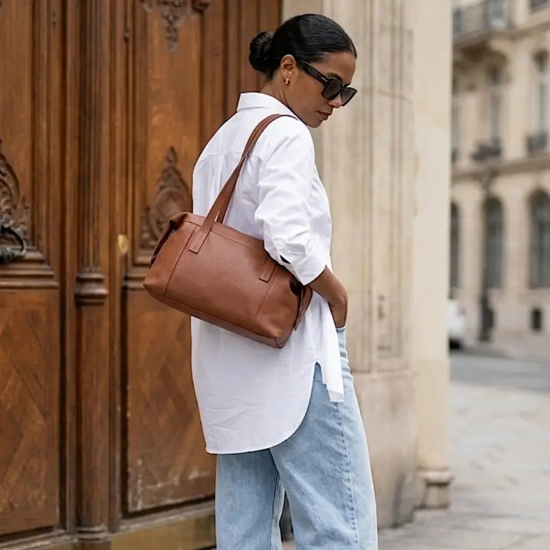 Mulher usando a bolsa tote feminina em couro legitimo no ombro, demonstrando o conforto da alça.