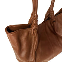 Mulher de look claro usando a bolsa de ombro tote caramelo, destacando o caimento elegante com o vão livre de 30cm da alça.
