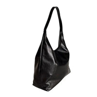 Vista lateral da bolsa estilo sacola preta mostrando a profundidade de 12cm e o caimento maleável do couro preto.