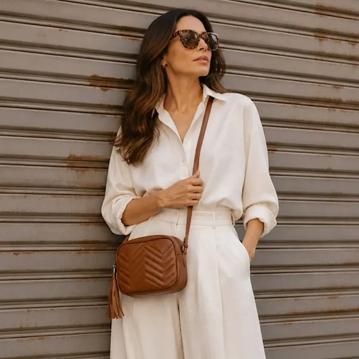 Mulher de look claro usando a bolsa transversal caramelo cruzada no peito, destacando o contraste.