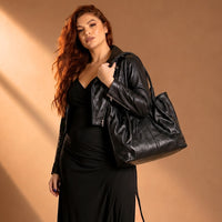 Mulher de blazer usando a bolsa de ombro tote preta, destacando o caimento elegante com o vão livre de 30cm da alça.