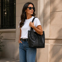 Mulher de blazer usando a bolsa de ombro grande preta, destacando o caimento macio do couro e o vão livre de 21cm.