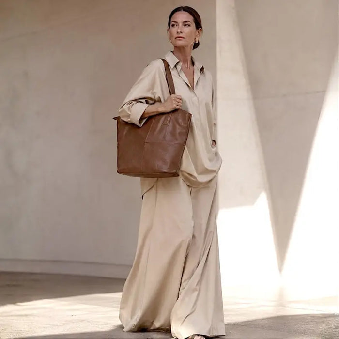 Mulher usando a bolsa de ombro grande marrom, evidenciando o caimento leve e o encaixe perfeito da alça de 3cm.