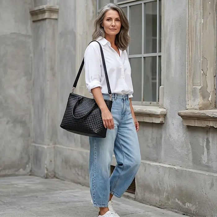 Look Jeans e Camisa Branca Usando a Bolsa shopper feminina preta com textura tressê em couro vegano e alças de ombro.