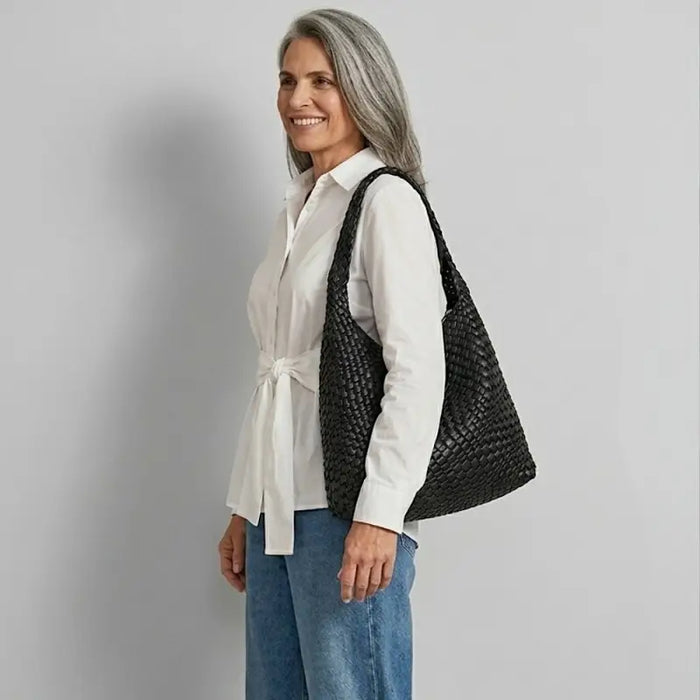 Mulher usando calça jeans baloon e camisa branca ampla com bolsa tressê feminina no ombro em couro vegano preto