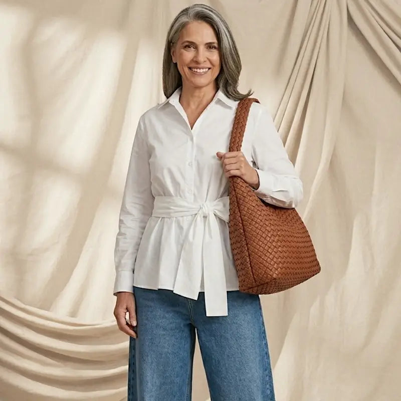 Mulher usando calça jeans baloon e camisa branca ampla com bolsa tressê feminina em couro vegano caramelo no ombro