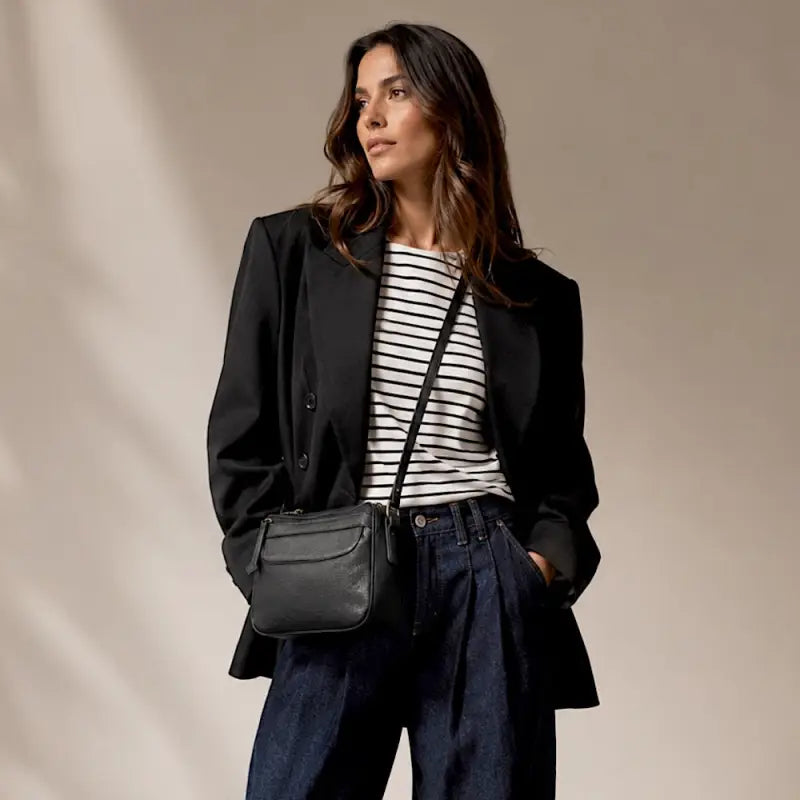 Mulher de blazer usando a bolsa crossbody preta ajustada na altura do quadril.