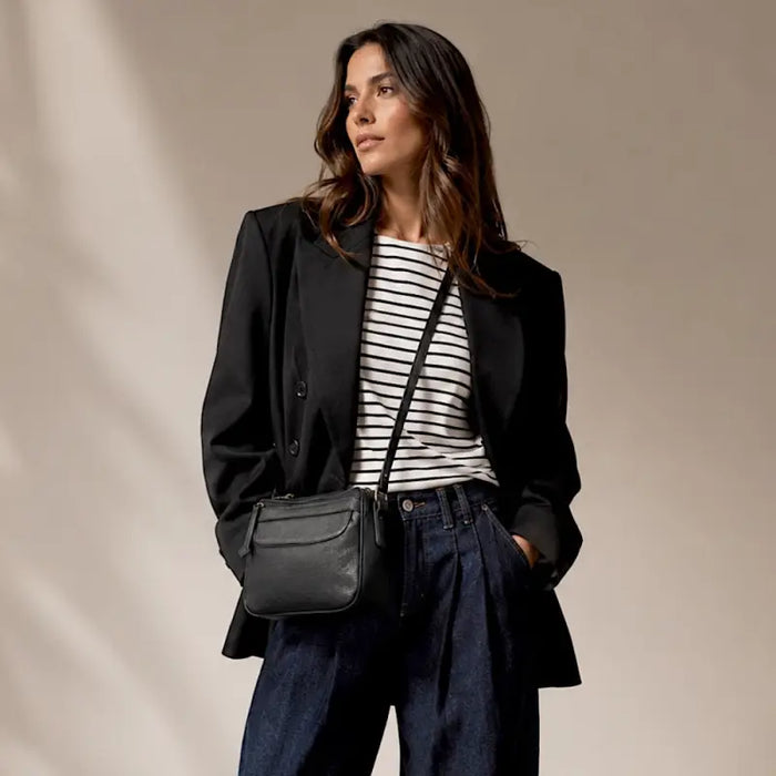 Mulher de blazer usando a bolsa crossbody preta ajustada na altura do quadril.