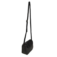Mulher de blazer com a bolsa crossbody preta apoiada ao lado no chão.
