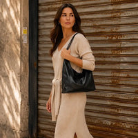Mulher usando a bolsa hobo grande preta encaixada perfeitamente abaixo do braço, destacando o estilo clean.